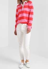 Czerwono-różowa, w paski koszulka polo z długim rękawem, z białym kołnierzykiem, zestawiona z białymi slim-fit dżinsami i białymi butami wsuwanymi.