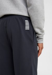 Pantaloni jogger blu navy con una vestibilità rilassata, dotati di una tasca laterale e dettagli con strisce verticali bianche sulla gamba. Realizzati in morbido cotone.