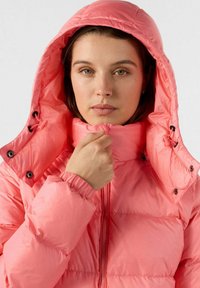 Giacca puffer corallo con colletto alto e cappuccio regolabile. Presenta polsini elasticizzati, chiusura con zip e finitura opaca. Design leggermente trapuntato.