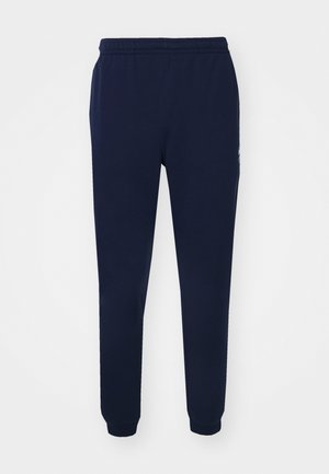 Marineblauwe joggpants van zacht materiaal, met een elastische tailleband, taps toelopende pijpen en ribgebreide boorden bij de enkels. Minimalistisch merkdetail.