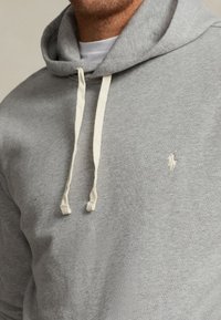 Felpa con cappuccio grigia in morbido misto cotone, con coulisse beige e un piccolo logo sul petto. Vestibilità standard, polsini a coste.