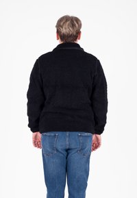 Zwarte fleece pullover met een gestructureerd oppervlakte, met een hoge kraag. Gekocht met blauwe spijkerbroek, zicht van achter.