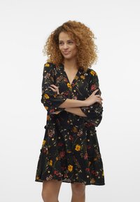 Vestido preto floral com mangas longas, apresentando uma saia em camadas e padrões vibrantes de flores em amarelo, vermelho e verde. Adequado para uso casual.