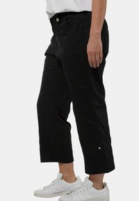 Pantalons noirs cropped en tissu léger, dotés de poches latérales et d'accents de boutons à l'ourlet, associés à des baskets blanches.