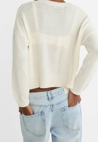 Cream knitted sweater with a cropped fit and ribbed hem, paired with light blue high-waisted jeans featuring large back pockets.