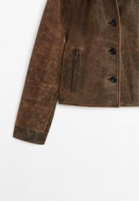 Giacca di pelle marrone con un design strutturato, dotata di quattro chiusure a bottone, una tasca con zip e tessuto testurizzato.