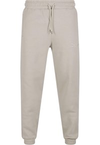 Light beige joggers made of soft fabric, featuring an elastic waistband and cuffs, side pockets, and a subtle embroidered logo detail.