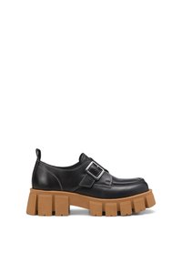 Des chaussures en cuir noir avec une semelle épaisse marron, présentant un accent de boucle latérale et des coutures blanches. Conçues avec un bout arrondi.