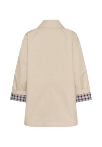 Manteau beige à manches longues avec poignets repliés dévoilant une doublure à carreaux noir et blanc, ourlet droit et un design simple de couture au dos.