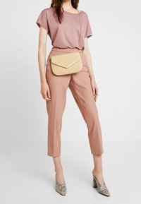 Light pink, short-sleeve, shiny top paired with tailored, pink trousers and a yellow woven crossbody bag, featuring a fold-over flap and chain strap.