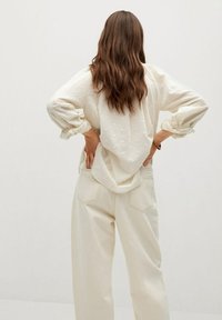 Cremfarbene Bluse mit strukturierten Pünktchen und voluminösen Ärmeln, kombiniert mit cremefarbenen, hochgeschnittenen Hosen mit Gesäßtaschen.