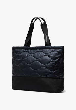 Sort quiltet tote-taske med bølgende syning, glat bundpanel og lange sorte håndtag, hvoraf det ene er trykt med teksten "Peak Performance".