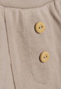 Beige tyg med en mjuk textur, med två runda gula knappar och synliga sömmar som accentuerar detaljerna på ett ficka.