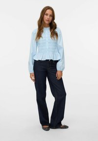 Lyseblå smocked bluse med lange ærmer og peplum kant, parret med mørke denim flared jeans og mønstrede flade sko.