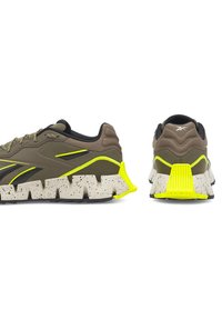 Brūni sporta apavi ar teksturētu virsmu, dzelteniem akcentiem un masīvu baltu raibumu zoli. Iezīmējas ar izturīgu dizainu.