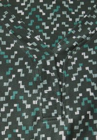 Groene stof met een zigzagpatroon in wit en teal. Kenmerkt zich door een V-halsontwerp en naaddetails. Zachte, lichte textuur.