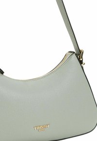 Borsa a mano verde in pelle con silhouette curva, hardware dorato e zipper visibile. Nome del brand "TWINTSET" impresso sul fronte.