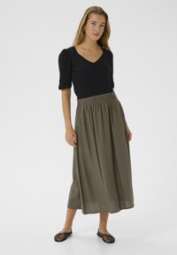 Haut noir à manches bouffantes avec un décolleté en V. Jupe kaki, longueur cheville avec une taille élastique. Chaussures slip-on en mesh noires.