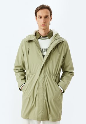 Veste imperméable vert clair avec une capuche doublée, une taille à cordon de serrage et des poches latérales. Caractérisée par une texture lisse et un design minimaliste.