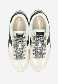 Ljusbeiga sneakers med svarta detaljer, texturerat mocka- och meshmaterial, med mönstrade svarta och vita skosnören samt en logotyp-etikett.