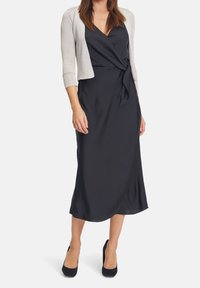 Svart klänning med omslag, djup V-hals, texturerad silverkofta, knälång, matchad med svarta högklackade skor. Slät tyg, minimalistisk design.