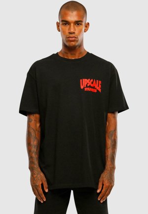 Black cotton t-shirt featuring red "UPSCALE" text on the left chest. Short sleeves, relaxed fit, minimalistic design without patterns.