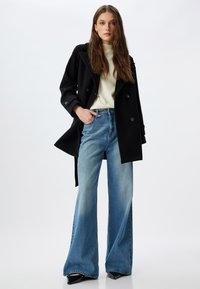 Dobbeltradet sort frakke over en cremefarvet sweater, parret med højtaljede, lyseblå flare jeans og sorte spidse hæle.