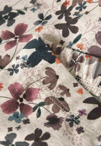 Primo piano di un tessuto beige con stampe floreali multicolori e cuciture visibili sui bordi piegati.