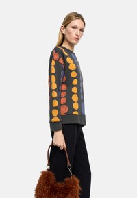 Ciemna bluza z dużymi pomarańczowymi, fioletowymi i żółtymi kołami. Miękka tkanina, okrągły dekolt i ściągacze na rękawach. Brązowa futrzana torebka z skórzanymi uchwytami.