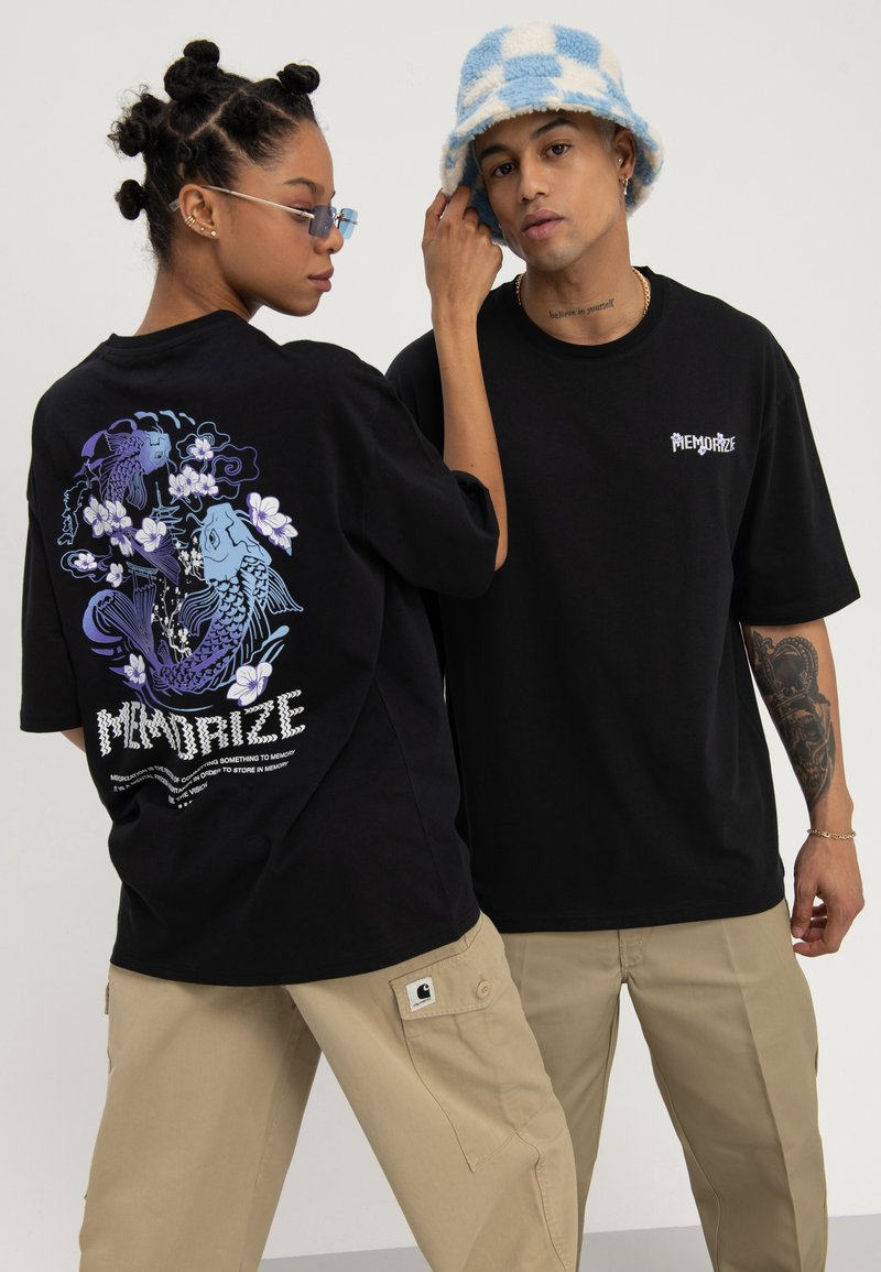Zwei Models tragen schwarze "MEMORIZE" T-Shirts, eines zeigt ein Koi-Fisch-Design auf dem Rücken, kombiniert mit beigen Cargohosen und Accessoires.
