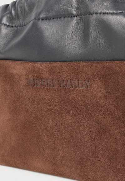 Material de velur maro cu logo-ul embosat "PIERRE HARDY" sub un material de piele neagră cu cusături vizibile.