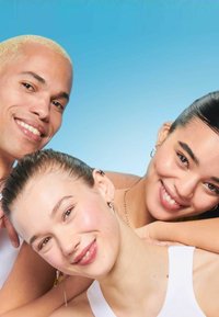 Trois personnes sourient, avec différentes couleurs de cheveux : l'une a des cheveux blonds, une autre a des cheveux noirs coiffés en arrière, et la troisième a une queue de cheval.