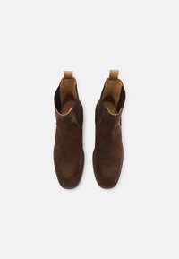 Bruine suède enkellaarzen met ronde neuzen, elastische zijkanten en een trekhaak. Beschikt over een gladde binnenvoering en gestikte zolen.