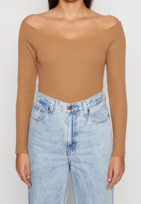 Brown ribbed long-sleeve top with an off-shoulder design, paired with light blue high-waisted jeans featuring a faded pattern and five pockets.