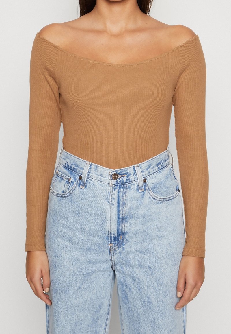 Brown ribbed long-sleeve top with an off-shoulder design, paired with light blue high-waisted jeans featuring a faded pattern and five pockets.