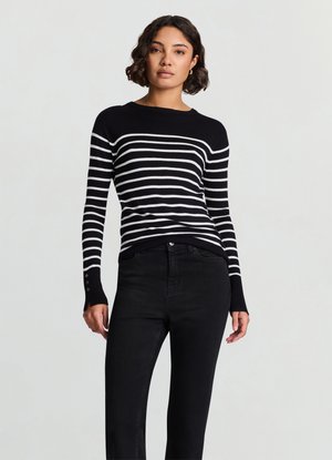 Pull rayé noir et blanc avec un col rond, manches longues avec des boutons aux poignets, associé à un jean noir.