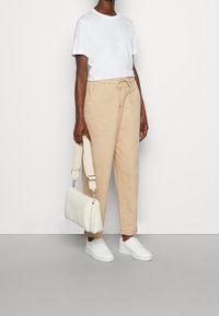 Witte crewneck t-shirt, beige drawstring broek en witte sneakers. Een getextureerde witte handtas met een schouderband wordt vastgehouden.