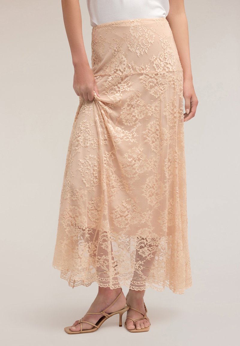 Fustă maxi din dantelă în piersică moale, având modele florale, margine ondulată și talie ajustată; textura transparentă sporește eleganța.