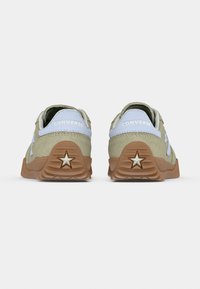 Par beige Converse-sneakers med gummisåler, stjerne-logo på hælen og lyseblå accenter på den bageste krave.