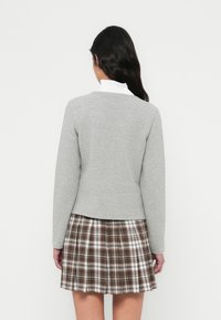 Γκρι πλεκτό πουλόβερ με μακριά μανίκια και στρογγυλή λαιμόκοψη, σε συνδυασμό με πλισέ καρό φούστα σε καφέ, λευκές και πορτοκαλί αποχρώσεις.