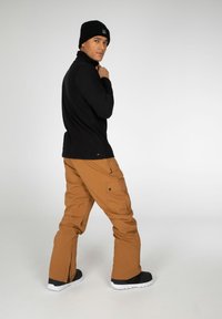 Maglietta nera a maniche lunghe, pantaloni cargo marroni con tasche e stivali neri. Design semplice, vestibilità rilassata, con un focus su funzionalità e comfort.