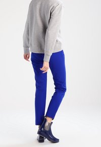 Grauer Sweatshirt mit Rundhalsausschnitt, kombiniert mit leuchtend blauen Hosen. Schenkelhohe, glänzende marineblaue Stiefel mit elastischen Seitenpaneelen.
