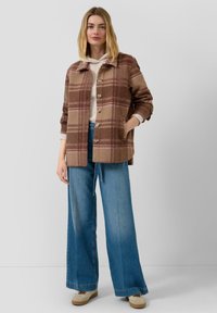 Braune kariertes Wolljacke mit Knöpfen, ausgestattet mit einem Hemdkragen und Seitentaschen, kombiniert mit weit geschnittenen blauen Jeans.