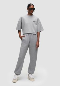 Grijze oversized sweatshirt met korte mouwen en logo, gecombineerd met bijpassende grijze joggingbroek, gedragen met witte sneakers en zwarte zonnebril.