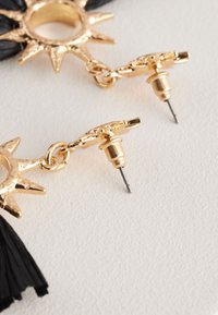 Gold-tone earrings with sun-shaped hardware and black tassel accents. Features a stud and post closure for secure wear.