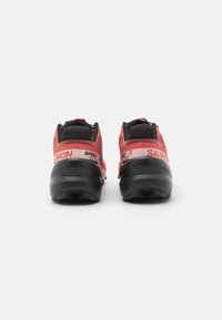 Pantofi de alergare pe traseu roșii și negri, cu un material superior din plasă texturată, guler căptușit și outsole din cauciuc agresiv pentru tracțiune. Include logo-ul brandului și numele modelului.
