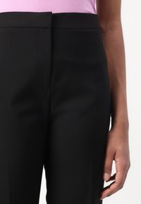 Pantaloni neri su misura con una vita media, davanti liscio e tessuto morbido. Il tessuto ha una leggera lucentezza, evidenziando le linee pulite.
