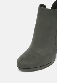 Bottine en daim gris foncé avec un bout arrondi et une semelle basse, vue en gros plan sous un angle avant latéral sur un fond blanc.