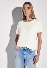Hvid T-shirt med korte ærmer og rund halsudskæring, båret over lyseblå denimjeans. Glat stof med en afslappet pasform. Enkel design.