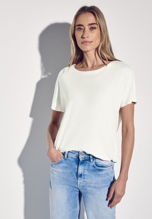 Weißes T-Shirt mit kurzen Ärmeln und Rundhalsausschnitt, getragen über hellblauen Denim-Jeans. Glatter Stoff mit lockerer Passform. Einfaches Design.